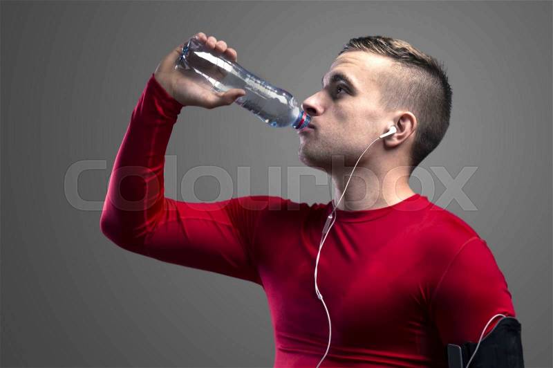 Young runner drinking water. Studio shot on a gray background, stock photo
