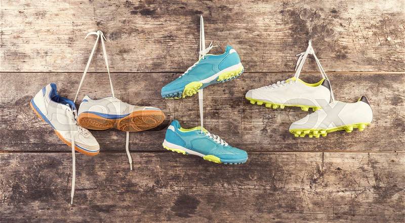 Three pairs of sports shoes hang on a nail on a wooden fence background, stock photo