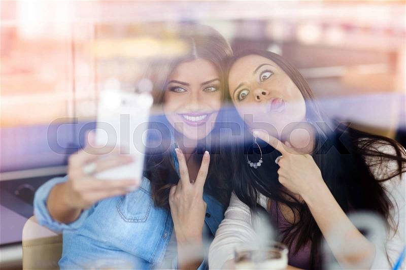 Two young beautiful women with smartphone in cafe , stock photo