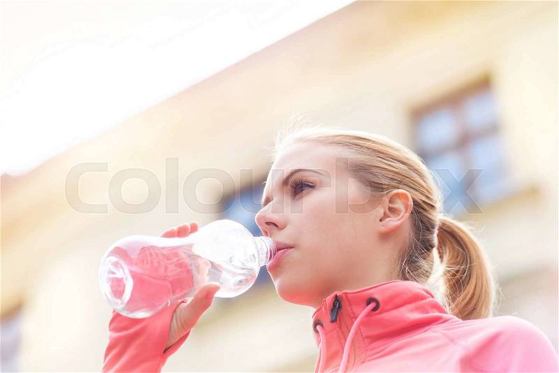 Beautiful young woman running in the city competition drinking water at the refresment point, stock photo