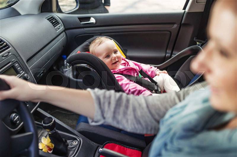 Mother driving a car, having her little baby girl in a child seat, stock photo
