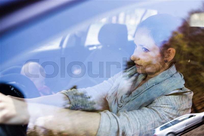 Mother driving a car, having her little baby girl in a child seat, stock photo