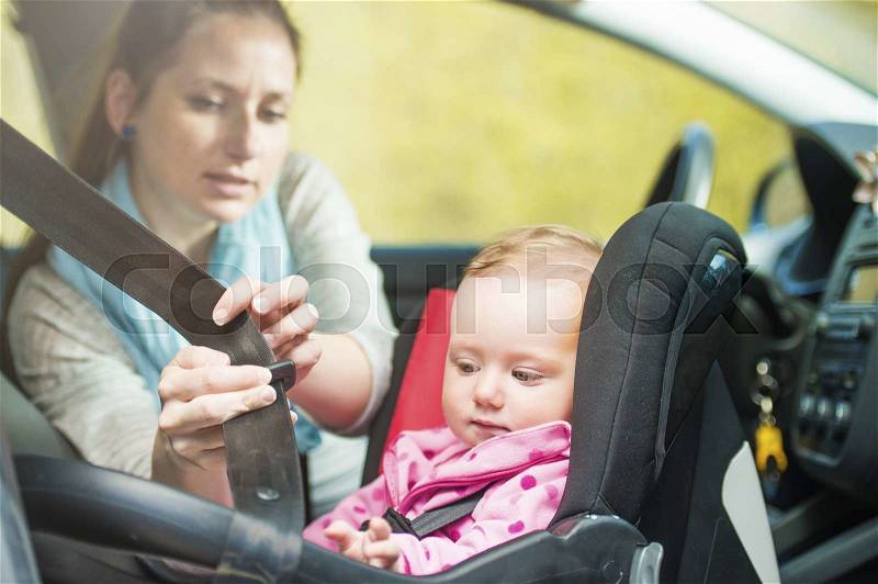 Mother in a car, having her little baby girl in a child seat, stock photo