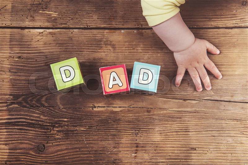 Little baby with cubes with dad sign on wooden background, stock photo