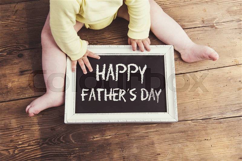 Little baby with Happy fathers day sign on wooden background, stock photo
