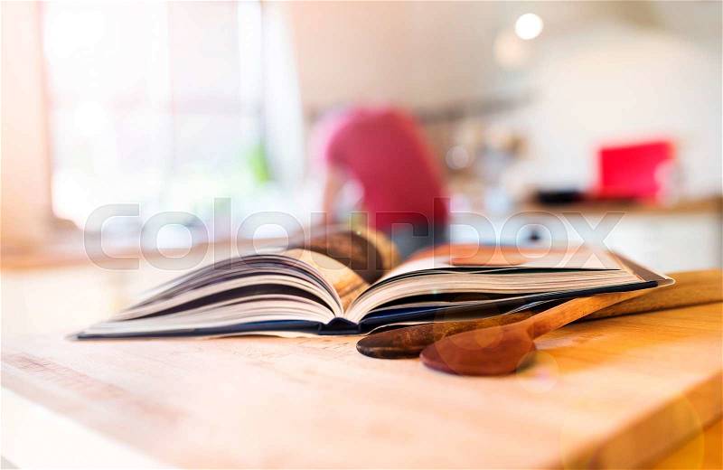 Cook book laid on a kitchen table with two wooden spoons, stock photo