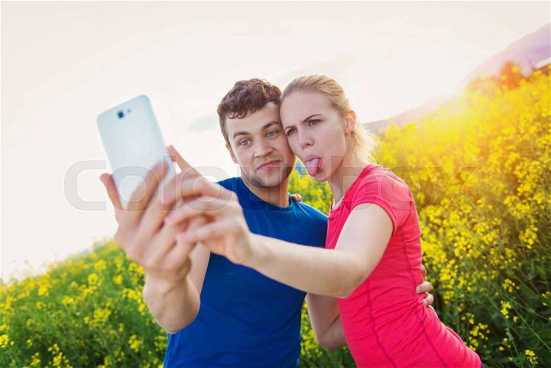 Young runners outside in spring canola field taking selfie with smart phone, stock photo