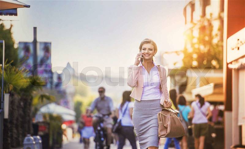 Attractive young business woman with smart phone walking in the city, stock photo