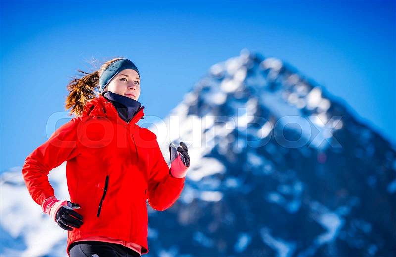 Young woman jogging outside in sunny winter mountains, stock photo