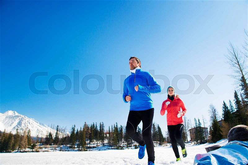 Young couple jogging outside in sunny winter mountains, stock photo