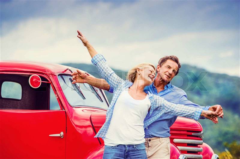 Senior couple standing by their vintage red car, stock photo