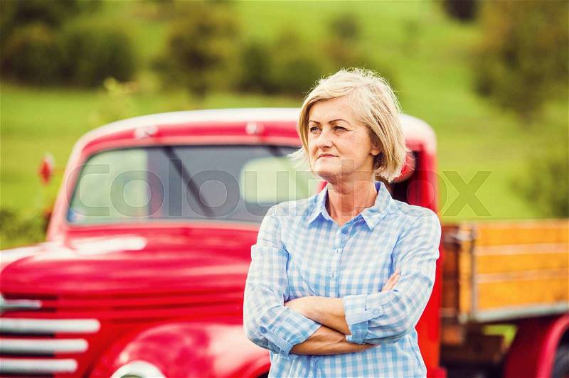 Senior woman standing by their vintage red car, stock photo