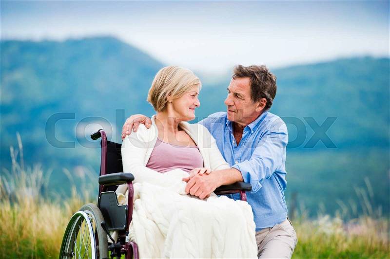 Senior man with woman in wheelchair outside in nature, stock photo