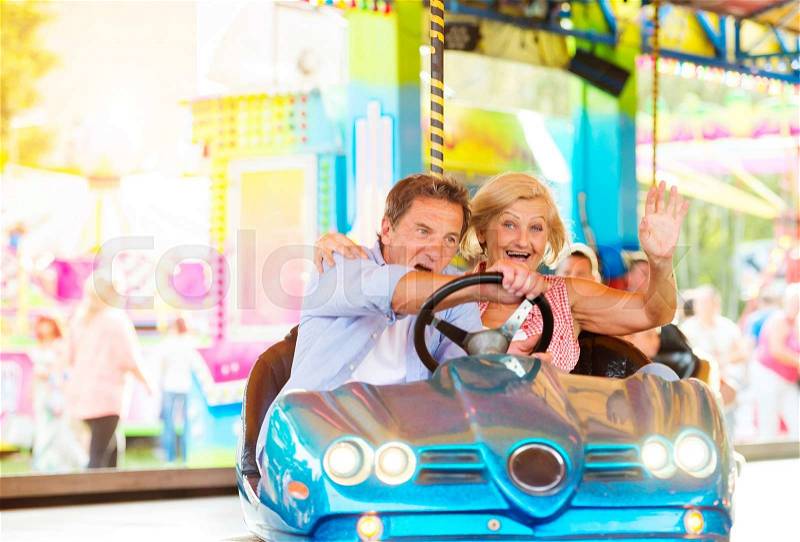 Senior couple having a ride in the bumper car at the fun fair, stock photo