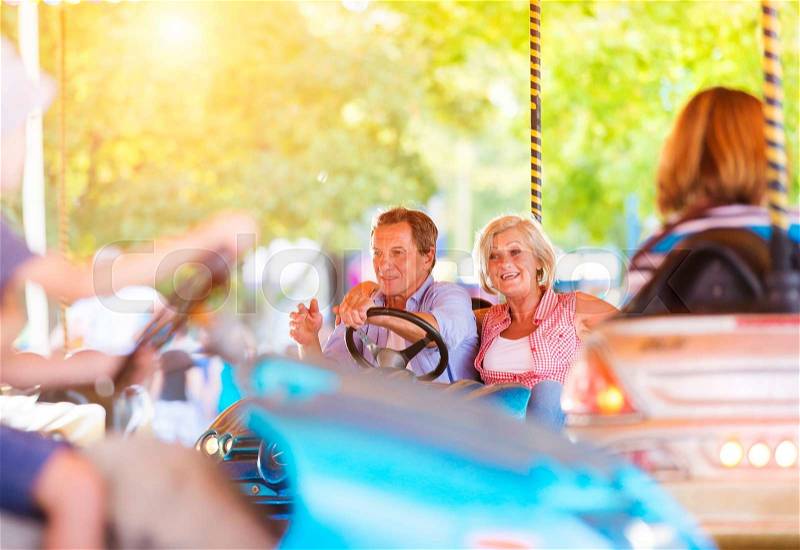 Senior couple having a ride in the bumper car at the fun fair, stock photo