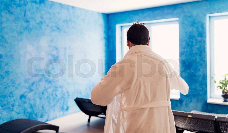 Man in white bathrobe sitting in lounge chair in spa room, stock photo