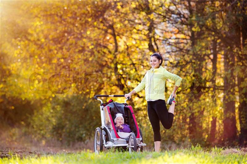 Beautiful young mother with her daughter in jogging stroller running outside in autumn nature, stock photo
