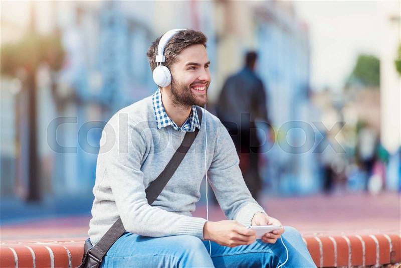 Handsome young man with white headphones outside in the town, stock photo