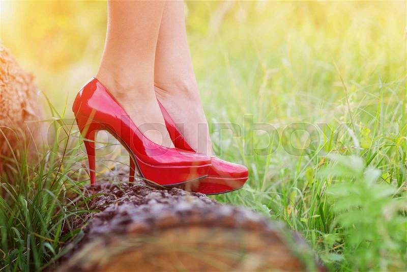 Unrecognizable young woman wearing red heels standing on a log, stock photo