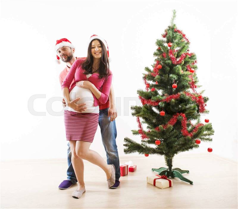 Young couple is dancing close to christmas tree. Woman is pregnant, stock photo