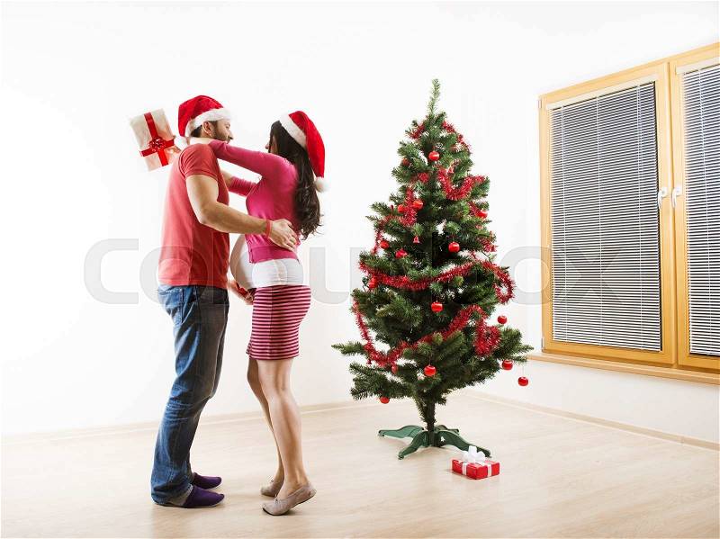 Young couple is dancing close to christmas tree. Woman is pregnant, stock photo