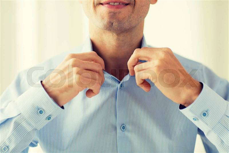 People, business, fashion and clothing concept - close up of smiling man dressing up and adjusting shirt collar at home, stock photo