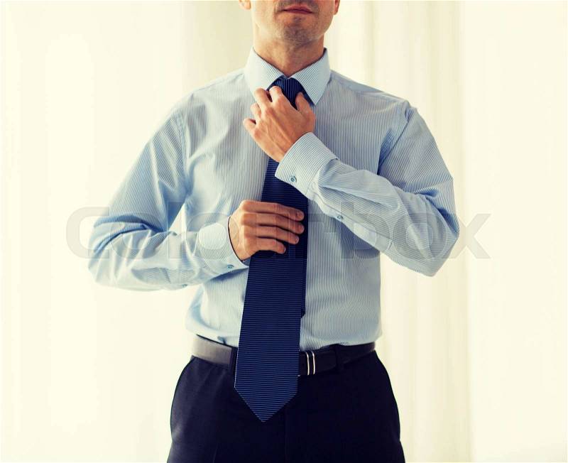 People, business, fashion and clothing concept - close up of man in shirt dressing up and adjusting tie on neck at home, stock photo