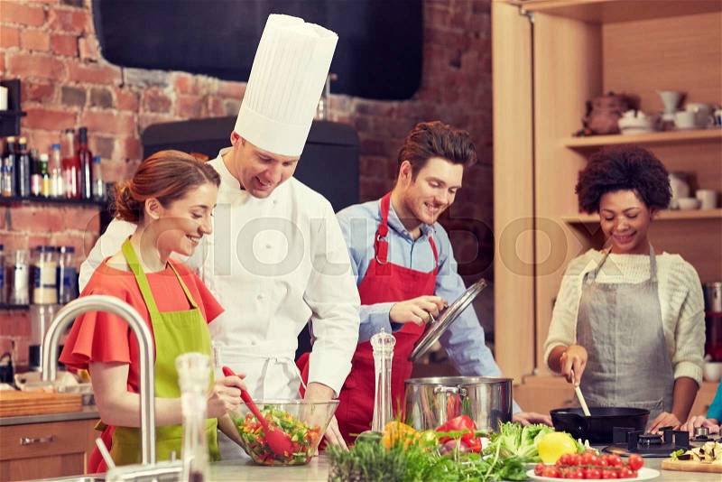 Cooking class, culinary, food and people concept - happy group of friends and male chef cook cooking in kitchen, stock photo