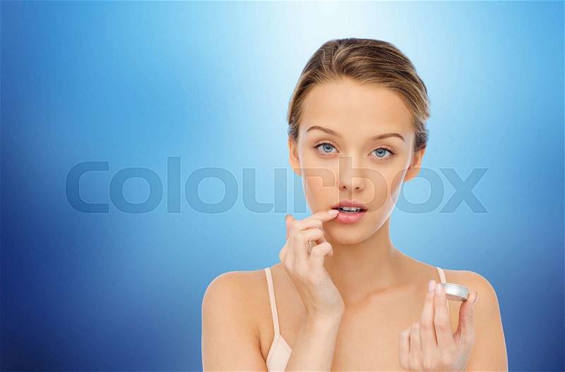 Beauty, people and lip care concept - young woman applying lip balm to her lips over marine blue background, stock photo