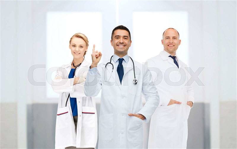 Healthcare, profession, people, gesture and medicine concept - group of happy doctors at hospital pointing finger up, stock photo