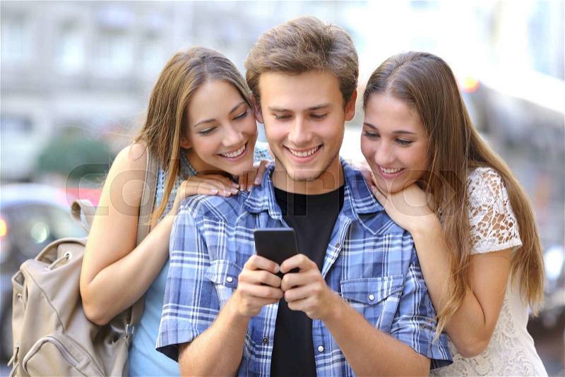 Funny friends sharing media in a smart phone in the street, stock photo