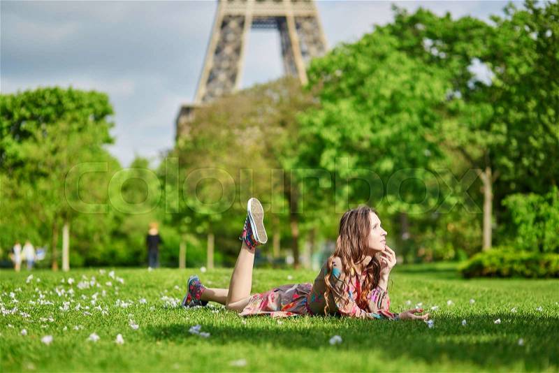 Beautiful young woman in Paris lying on the grass near the Eiffel tower on a nice spring or summer day, stock photo