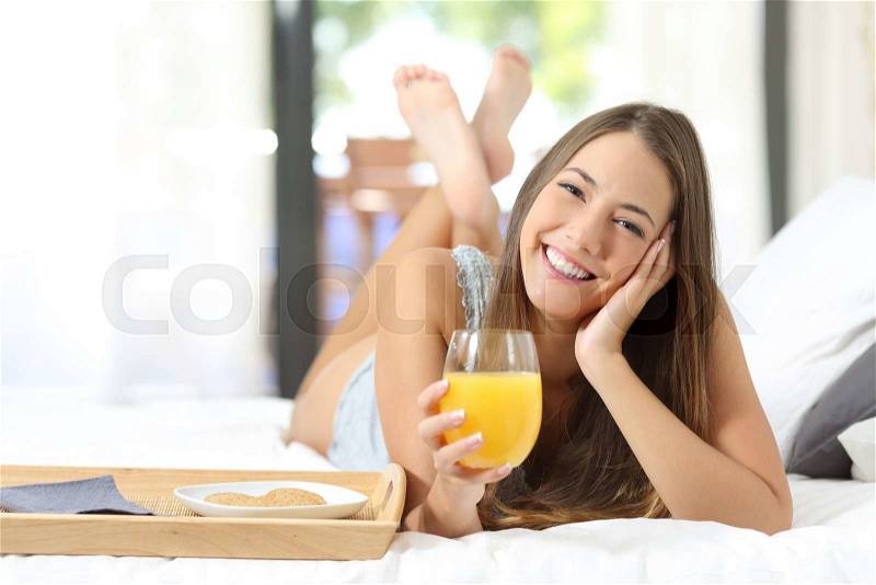 Happy girl having breakfast with orange juice on the bed at home and looking at camera, stock photo