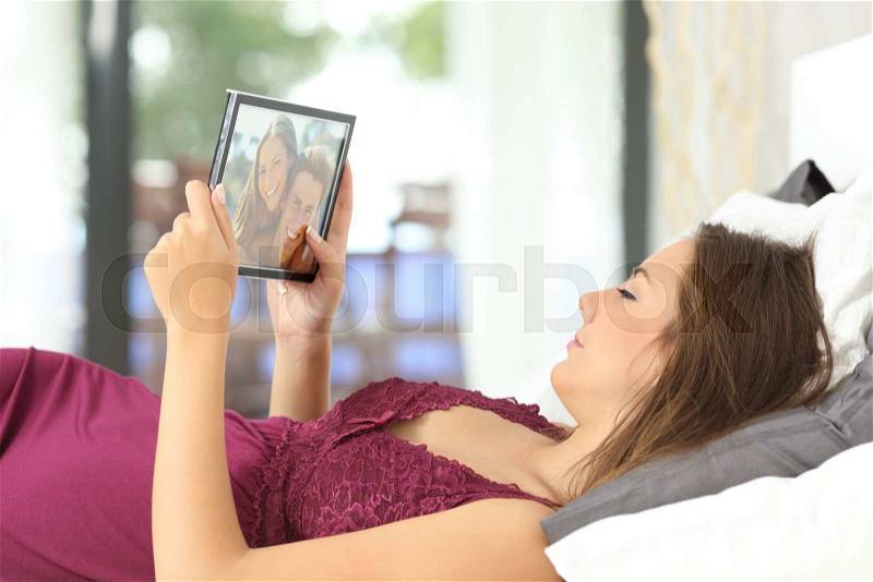 Longing woman looking a picture of her boyfriend in a frame on the bed at home, stock photo