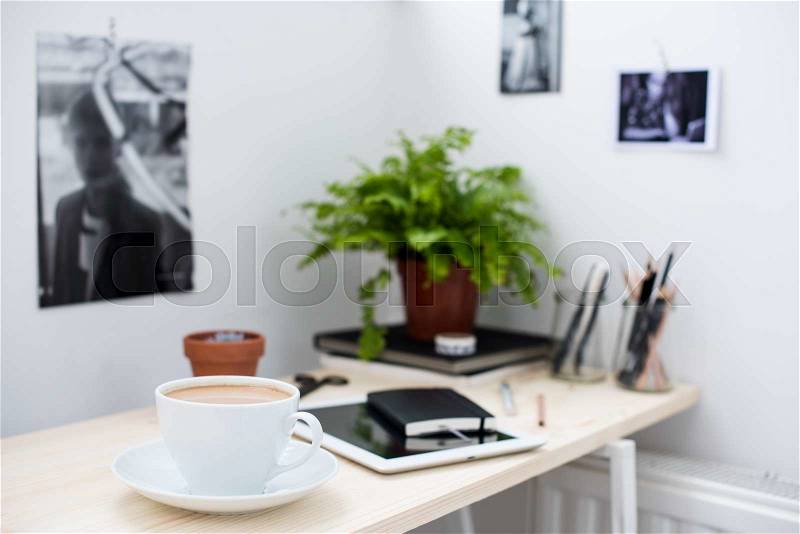 Cup of coffe in bright and modern loft-style office, work desk with office accessories. Digital gadgets, tablet and smartphone on the working table, stock photo
