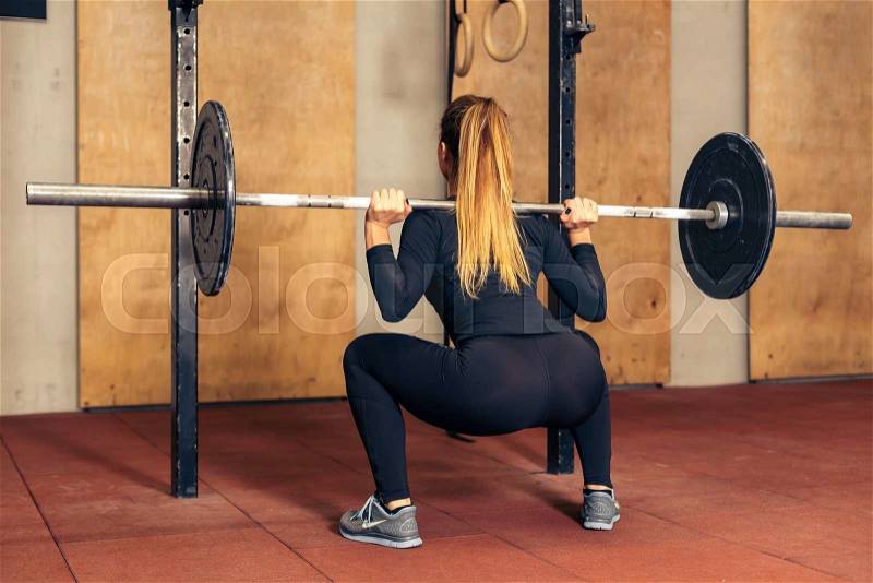 Back view young adult girl doing heavy duty squat in gym with barbell.Sexy woman with perfect abs doing squat exercises. Fitness blonde fit woman in great shape, stock photo