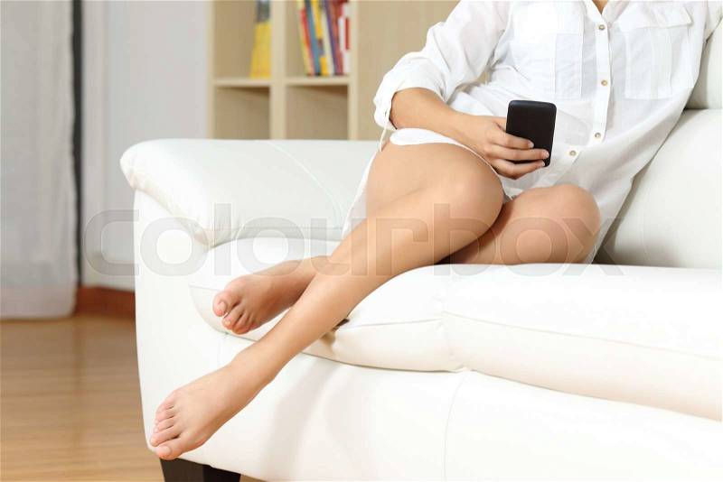 Woman resting on a couch using smart phone with waxed legs in foreground, stock photo