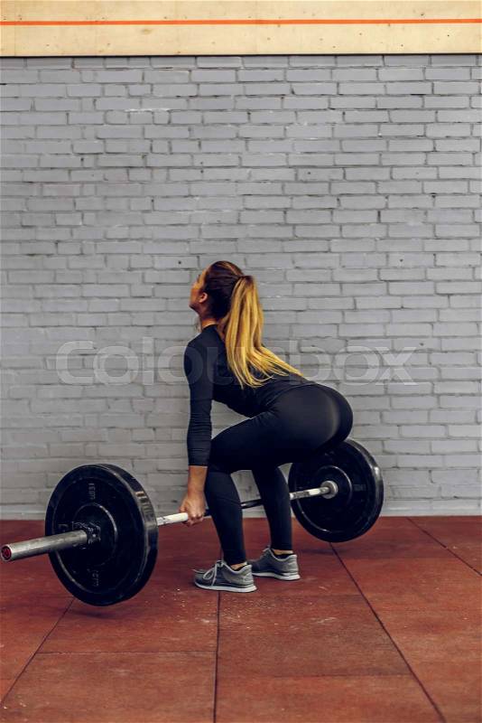 Strong young woman lifting heavy weights at gym. Fitness female in a black compression suit doing crossfit workout, stock photo