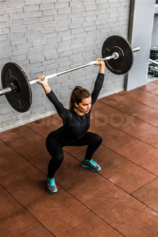 Fit young woman training squats with barbells over head with heavy weights at gym.. Strong girl lifting barbell as a part of crossfit exercise routine. , stock photo