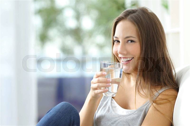 Girl drinking water sitting on a couch at home and looking at camera, stock photo