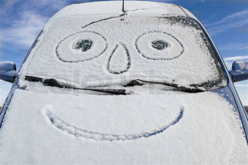 Car covered snow with drawn smiley in windshield against the blue sky, stock photo