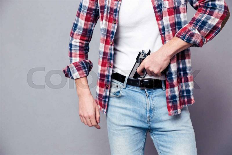 Closeup of gun holded by hands of strong young man in checkered shirt and jeans over grey background, stock photo