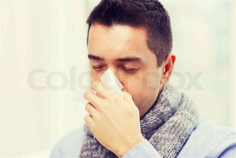 Healthcare, flu, people, rhinitis and medicine concept - close up of ill man blowing his nose with paper napkin at home, stock photo