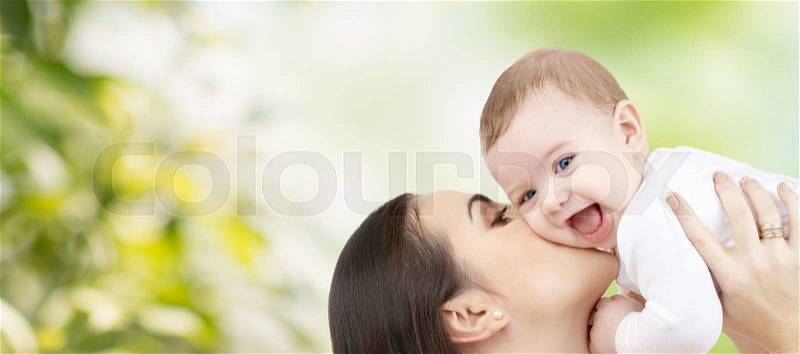 Family, motherhood, children, parenthood and people concept - happy mother kissing her baby over green natural background, stock photo