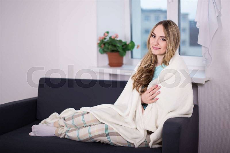 Winter concept -young woman in pajamas wrapped in blanket sitting in living room, stock photo