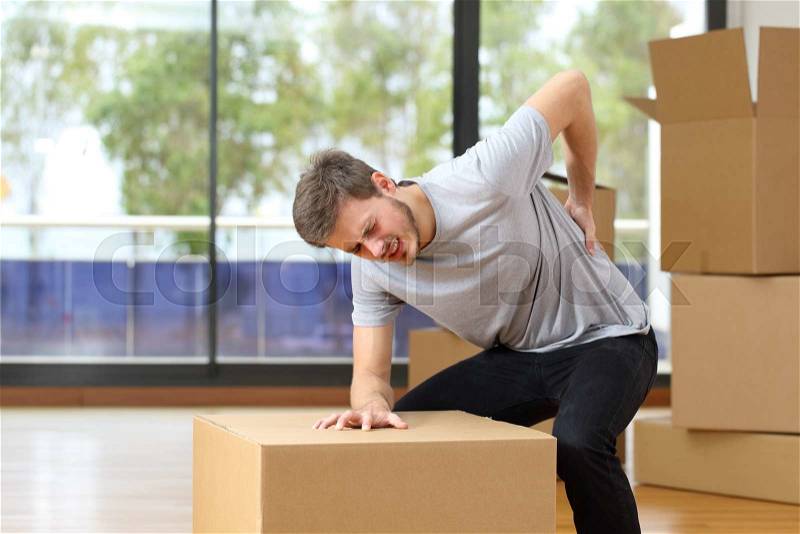 Man suffering back ache moving boxes in his new house, stock photo