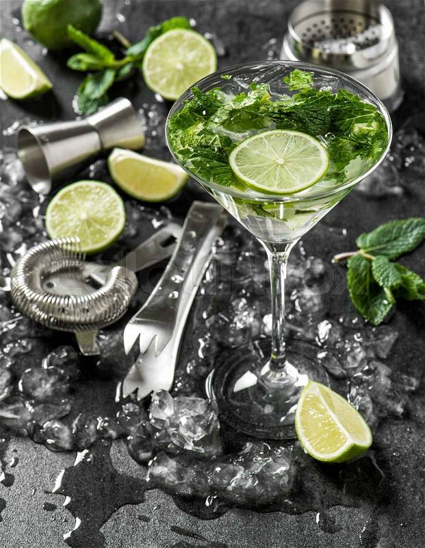 Cocktail drink with lime, mint and ice. Bar tolls and ingredients on dark background, stock photo