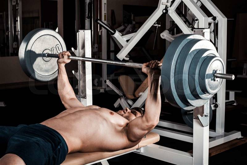 Muscular Man Doing Heavy Exercise. Athletic man pumping up muscles on bench press, stock photo