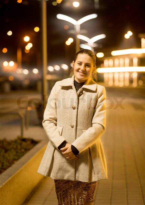 Portrait of happy elegant woman posing on street at night, stock photo