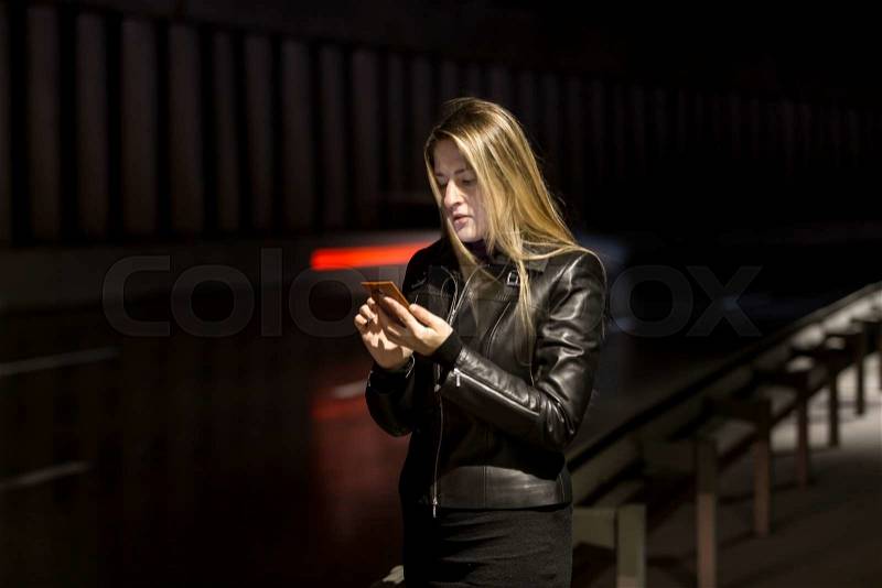 Night portrait of blonde girl using mobile phone on street, stock photo